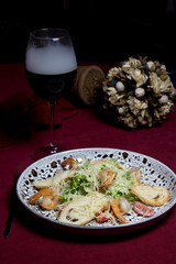 Vegetable salad with bread, shrimp and cheese. Near a glass of wine with smoke, flowers on a red tablecloth