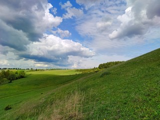 green field and mountain against the blue sky with large clouds on a sunny day