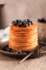 Round American pancakes with honey and blueberries for the holiday pancake week. Honey drips from the spoon directly onto the pancakes. A large freshly baked stack of pancakes