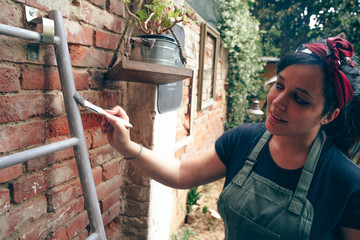 Young woman painting a metal ladder in the garden of her home. She's doing improvements during the Coronavirus Covid-19 quarantine.