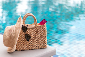 Weaving bag and hat with sunglasses and sunscreen lotion next to a swimming pool, summer travel concept