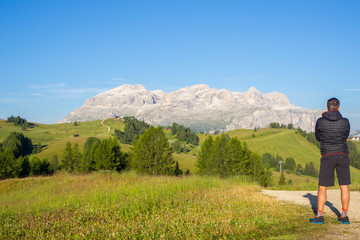 Obraz premium A person admires the fantastic Dolomites in Italy during the summer period. The massive Sella in the background. Hiker photographed from behind. Dolomites a Unesco World Heritage