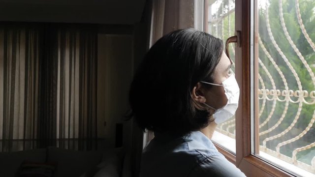 Young woman In medical mask is looking out window