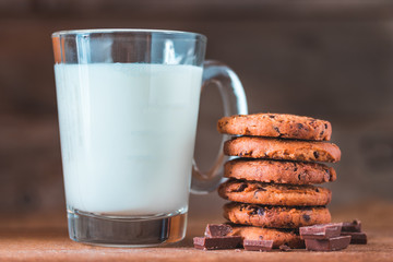 Chocolate chips cookies with crumbs and fresh milk on wooden background, homemade sweet and dessert concept