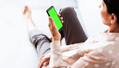 Middle-aged brunette woman on the gray sofa use green screen mobile phone smartphone.