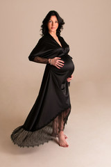 Naklejka premium Portrait shoot of young beautiful pregnant woman posing for maternity photoshoot lifestyle, pregnant belly. Stylish happy mother wearing a black elegant robes and to be waiting for a baby 
