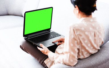 Middle-aged brunette woman on the gray sofa working on green screen laptop, soft focus, stay at...