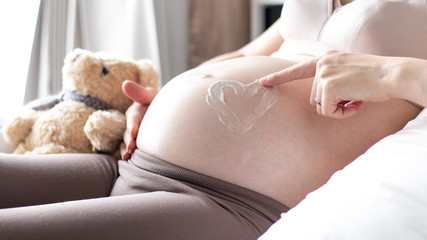 Close up shot of pregnant woman, heart shape stretch mark cream, mother expecting twins on a bed