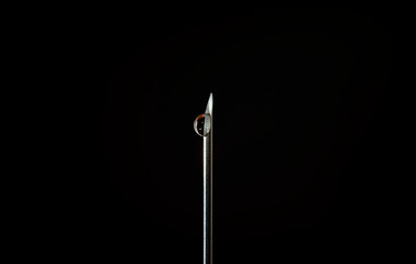 Medical syringe with a needle and drop on dark background 