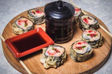 Rolls are laid out in a circle on a round wooden plate. In the middle of soy sauce.