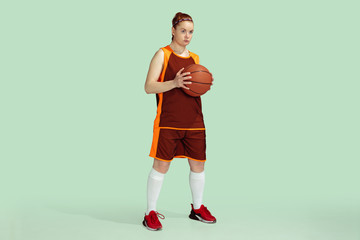 Young caucasian female basketball player confident holding ball, posing isolated on mint colored...