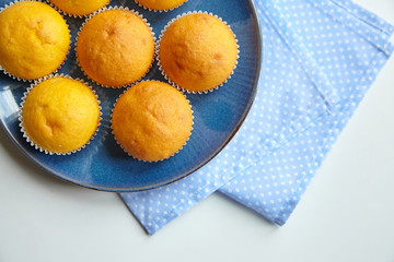 Pumpkin muffins on blue plate on white table, top view. Homemade bakery, plant-based food
