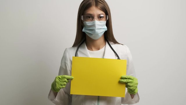 Female doctor in a mask of Caucasian appearance holds in her hands a yellow A4 sheet
