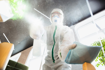 Coronavirus Pandemic. A disinfector in a protective suit and mask sprays disinfectants in house or...