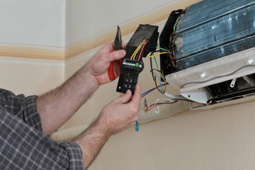 Electrician servicing air condition device in a room using pliers