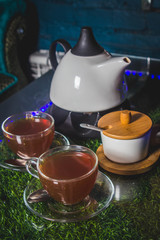 Tea-set. In front are two cups of tea. Behind the sugar bowl and kettle. On a glass table