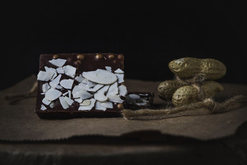 chocolate sprinkled with seeds. Nearby lies peanuts. Photo on a black background