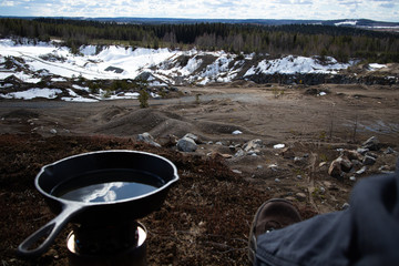 Cooking steaks and potatoes with cast iron frying pan next to sand pit at spring time.