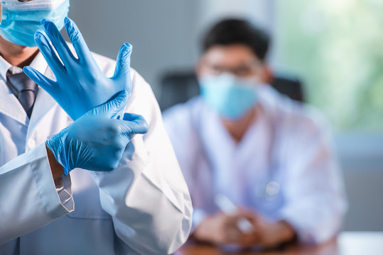 Asian doctors will wear blue medical gloves and medical masks to prevent coronary artery infections (Covid-19) in the doctor's office. The background is another Asian doctor who is currently working.