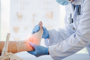 Asian orthopedist or orthopedic doctor Wear a surgical mask and medical gloves. We are examining the cause of the ankle bone. - obrazy, fototapety, plakaty