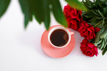 pink cup of coffee and three red peonies on the white background