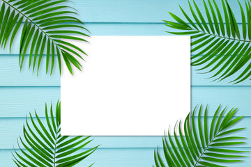 Fototapeta na wymiar top view of tropical palm leaf white paper note frame on blue wooden background, copy space minimal summer concept, flat lay