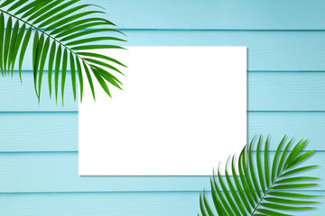 Fototapeta na wymiar top view of tropical palm leaf white paper note frame on blue wooden background, copy space minimal summer concept, flat lay