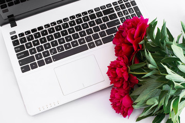 white laptop with black buttons and three red peonies
