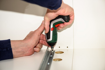Close up on hands with cordless screwdriver assembling furniture