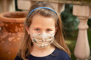 Ritratto di bambina bianco con mascherina protettiva in tessuto isolata su lo sfondo di un giardino