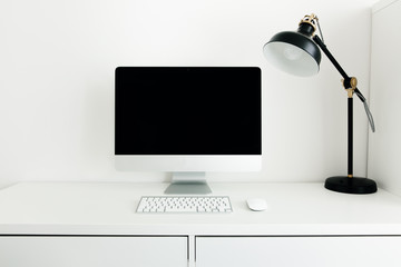 
White desktop with black monitor and desk lamp. Workplace concept. Mock up blank computer screen with keyboard. Minimalism in the interior.