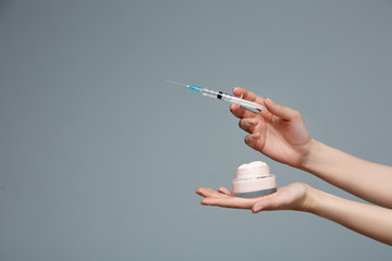 Female hands holding face cream and syringe with beauty injection, choosing skin care products....