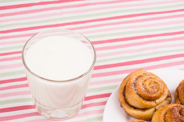 Freshly baked homemade snail buns with sugar and cinnamon on white plate and striped tablecloth with milk in glass. Balanced nutrition, proteins and carbohydrates, cereals