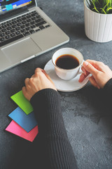 girl holds a coffee mug, a laptop stands next to it and stickers lie
