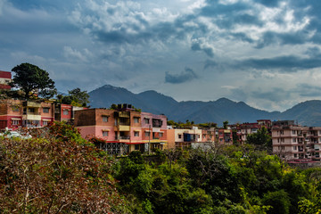 low angle shot of small town along side trees with mountains and cloudy blue sky in the background - Powered by Adobe