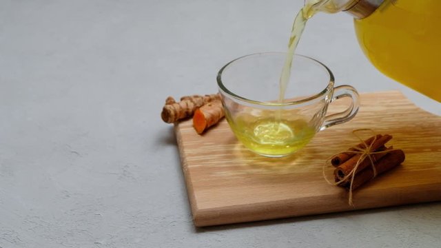 Immunity boost turmeric tea pouring into glass cup on neutral light background with space for text