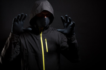 Masked thief is trying to scare you with raised arms isolated on black background