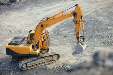 Small yellow excavator on a crawler in a stone quarry, close-up. Heavy mining equipment.