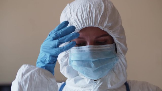 Portrait of exhausted female doctor taking off face mask and protective suit sighing in relief after working long hours at hospital. Tired medical worker. Health care.