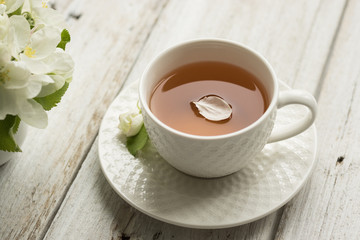 A cup of tea and a branch of a blossoming apple tree on the table. Flower petals in a drink