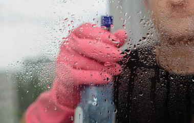 Fototapeta premium young guy in pink rubber gloves holds window cleaner and rag and washes plastic windows