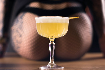 cocktail in a transparent glass on a background of beautiful buttocks. on the bar sits a girl with a bare ass. Close-up of a yellow drink.