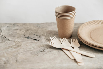 Wooden forks and paper cups with plates on wooden background. Eco friendly disposable tableware. Also used in fast food, restaurants, takeaways, picnics. Copy, empty space for text
