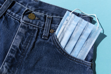Classic blue jeans on the white background. Medical mask in the pocket. Pandemic concept. Top view. Flat layout