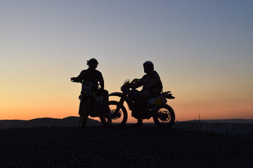 Fototapeta na wymiar two motorcyclists on a mountain ridge opposite sunset