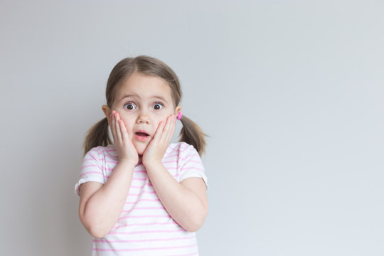 Portrait of a white girl 4 years old. She is very surprised, her mouth is open, her hands on her cheeks. Attractive. Discounts, sale. Grey background. Incredible. Place for text, layout.