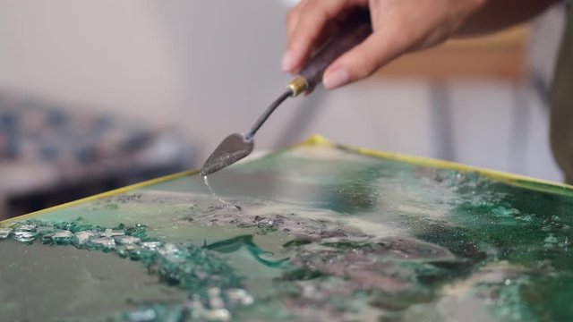 Artist holds palette knife. Person is drawing absract picture. Artist uses acrylic paints.