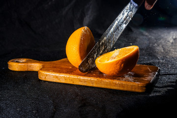 Orange are chopping by machete on wooden desk at black isolated background