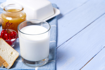 glass of milk with, honey and bread on light blue wooden background. Country breakfast food concept.