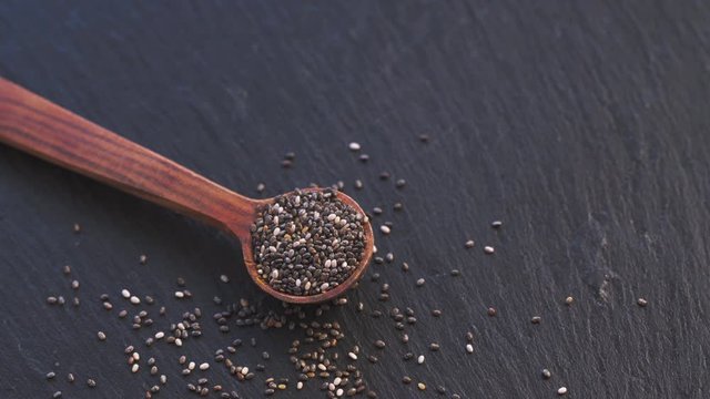 Rotation of chia seed in small wooden scoop on slate background